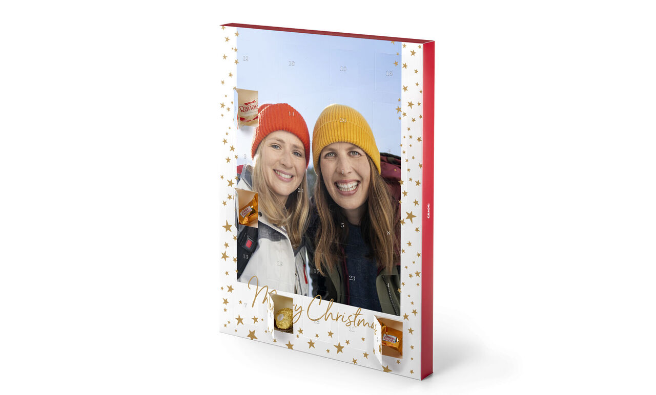 CEWE fotobok med juldesign, två personer håller den. Omslaget har gyllene stjärnor och texten 'Merry Christmas'.