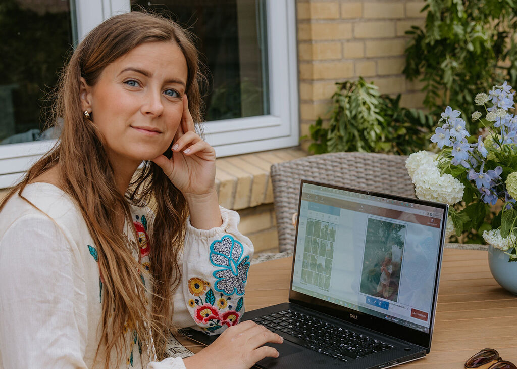 En person arbetar på en laptop utomhus omgiven av blommor i en avkopplande atmosfär.