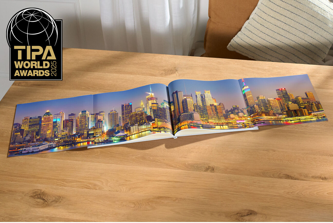 En öppen CEWE FOTOBOK med bilder på en stadsutsikt på ett bord, med ett fönster med gardiner i bakgrunden.